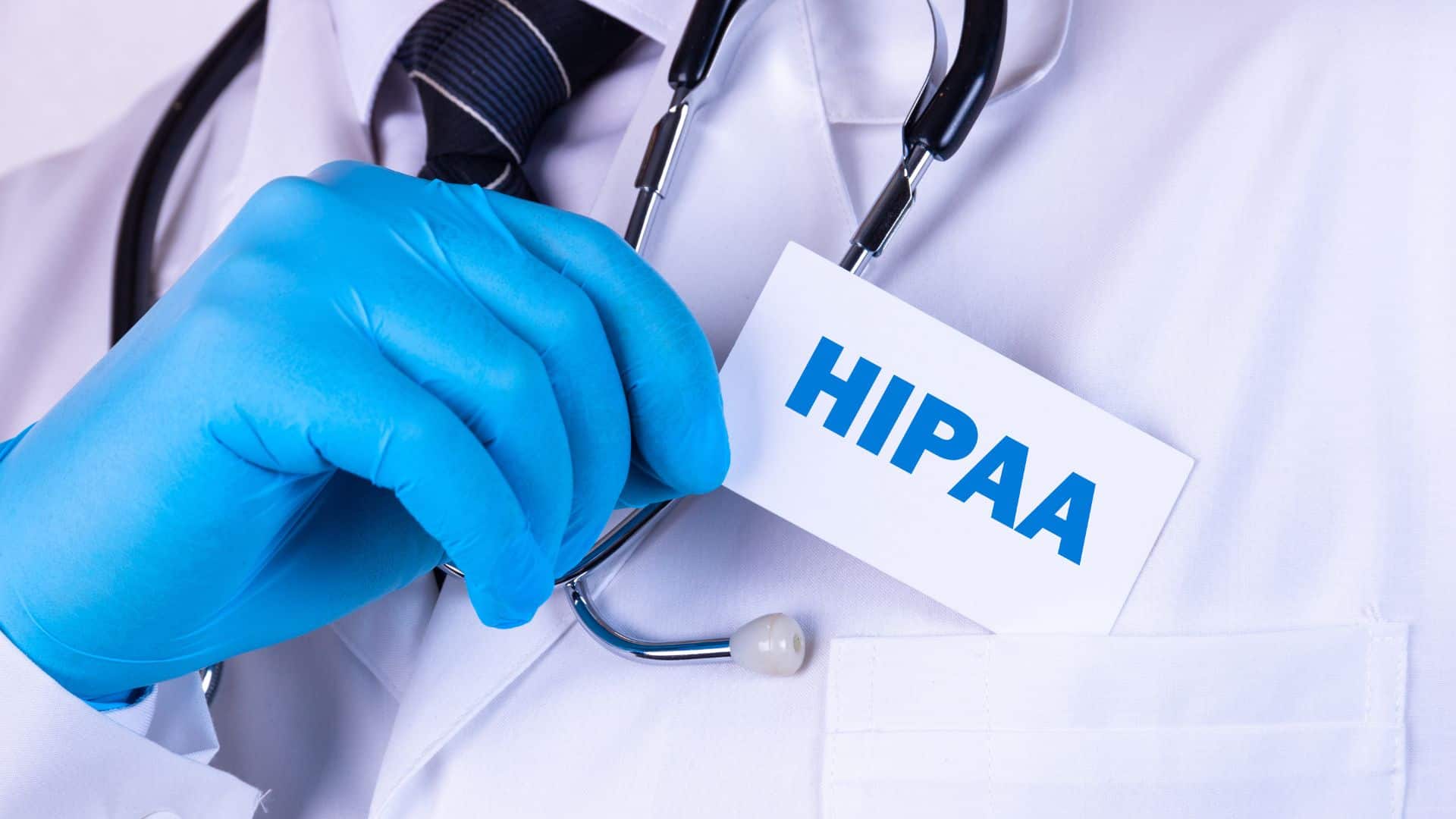A doctor in a white coat with a stethoscope, holding a card labeled HIPAA with gloved hands, emphasizing healthcare compliance.