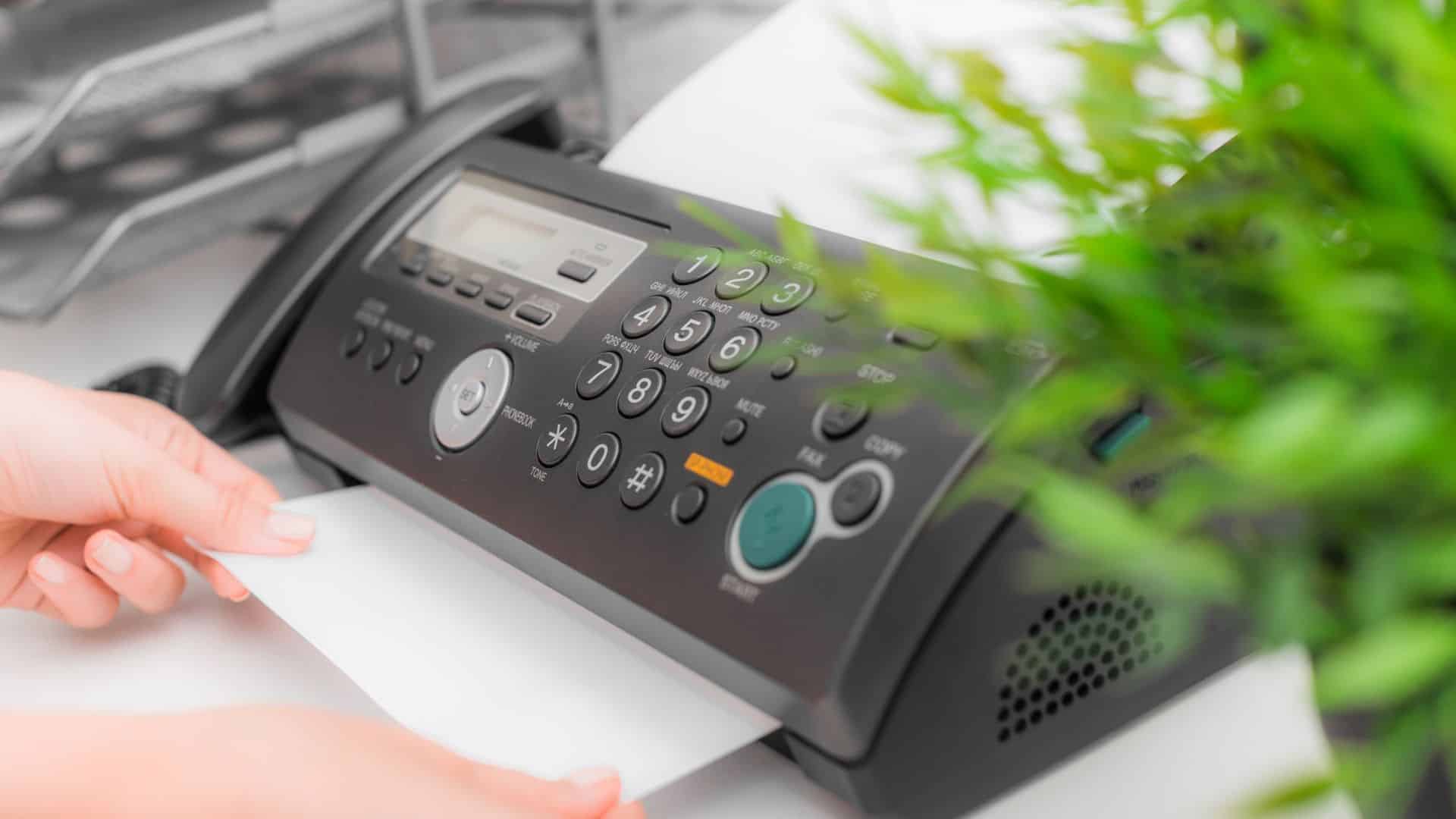 Hand placing document into traditional fax machine, symbolizing legacy fax technology.