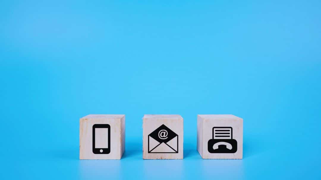 Three wooden blocks with icons on a blue background: a cell phone, an email envelope, and a fax machine, illustrating email to fax.