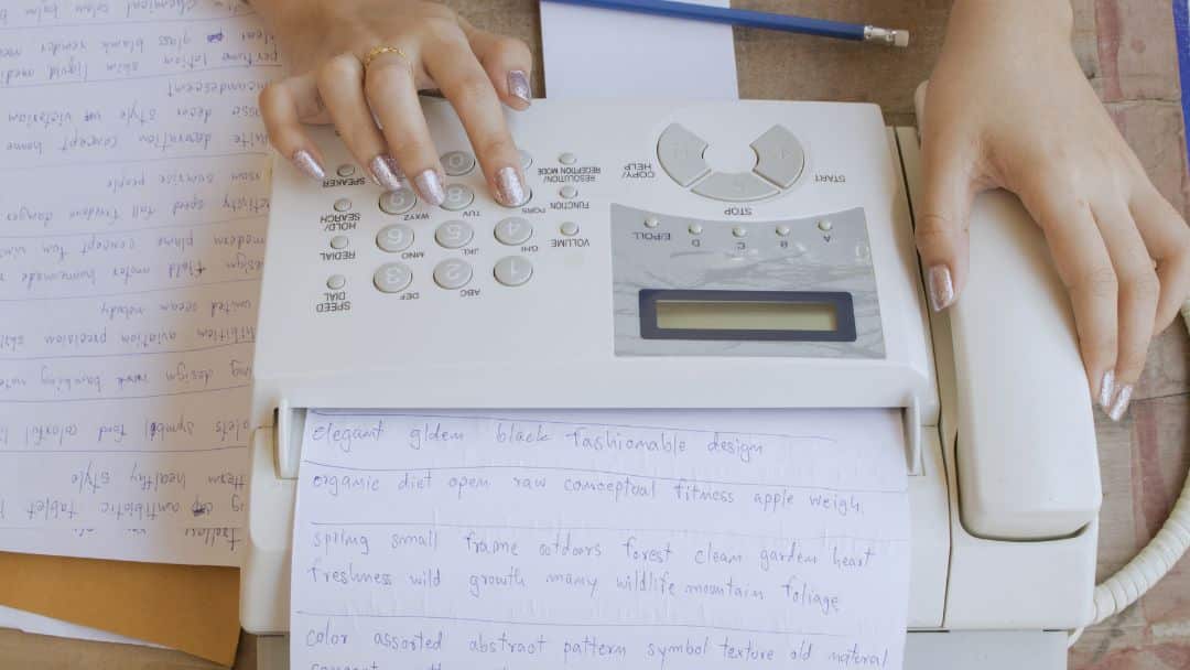 Hands dialing numbers on traditional fax machine surrounded by handwritten documents, revealing hidden costs of traditional fax most businesses still miss.
