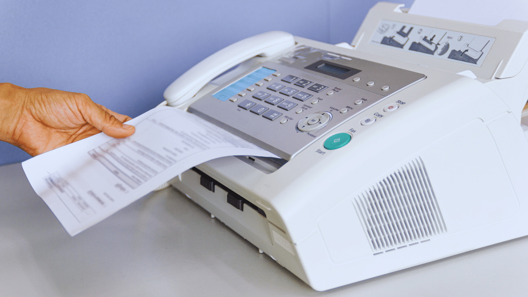 Hand pulling a printed document from a fax machine, representing the question of whether you can use your existing fax number with cloud fax.