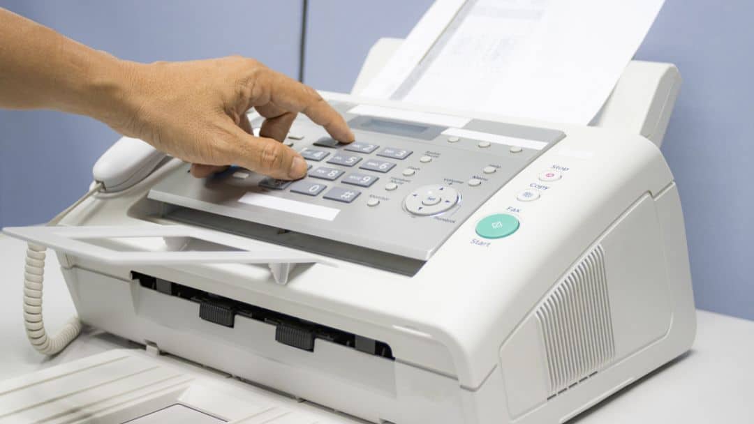 Traditional fax machine: hand dialing on keypad to send fax, paper in feeder, classic office device with Start/Fax buttons